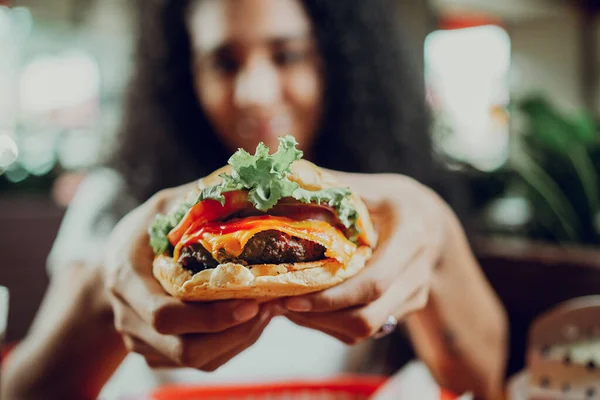 stock image Close-up of a girl showing appetizing hamburger in a restaurant. Hands of girl showing burger in a restaurant