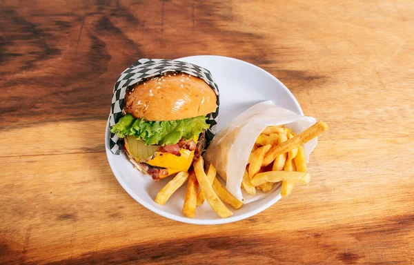 木製のテーブルにフライドポテトを添えた大きなチーズバーガー 木のテーブルの上の皿の上の美味しい自家製ハンバーガー — ストック写真