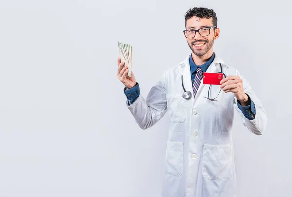 クレジットカードとお金を持っている幸せな若い医師 孤立したお金とクレジットカードを持っているハンサムな医師 — ストック写真