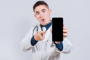 Şaşırmış genç doktor cep telefonu ekranını işaret ediyor. Latin doktor cep telefonu ekranında bir uygulama gösteriyor.