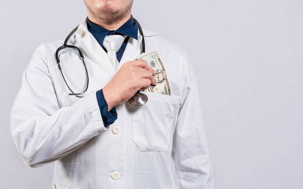 Dishonest doctor putting money in pocket. Corrupt doctor putting bribe money in pocket isolated. Medical bribery concept