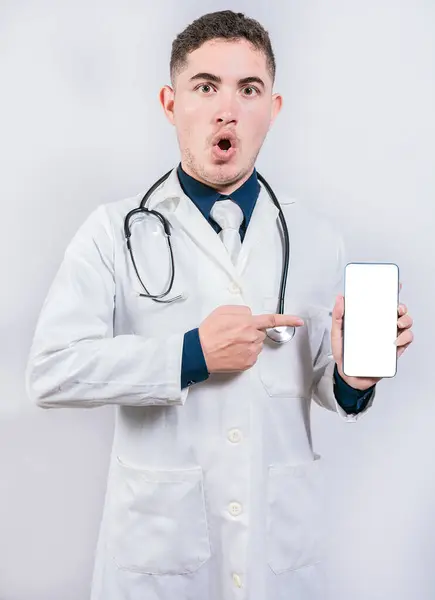 震惊的医生指着手机上的一个应用程序 令人惊讶的年轻医生手持和指向手机屏幕 — 图库照片