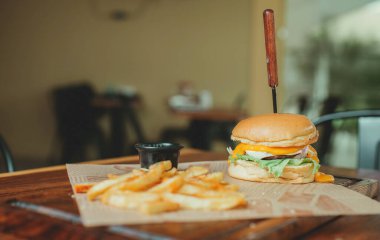 Tahta bir masada patates kızartması ve lezzetli bir hamburger. Patates kızartmalı çizburger, ahşap masada fotokopi alanı ile servis edilir.