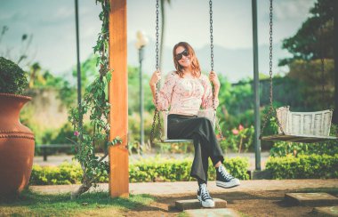 Doğa parkında salıncakta sallanan mutlu genç bir kadın. Doğa parkında salıncakta oturan gülümseyen bir kızın portresi.