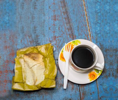 Top view of Tamal Pisque stuffed with a cup of coffee served on the table. Tamal Pisque stuffed typical Nicaraguan food. View of a stuffed tamale with a cup of coffee served on a wooden table clipart