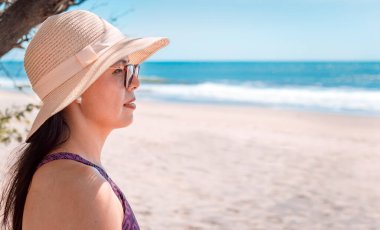 Pretty girl with a hat looking at the sea, close up of a woman looking at the ocean.