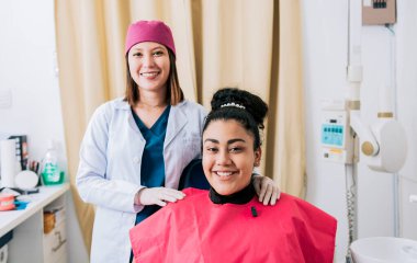 Kameraya gülümseyen memnun bir hastası olan dişi dişçi, dostane gülümseyen bir hastası olan dişi dişçi. Ofiste kameraya gülümseyen bir dişçinin portresi.