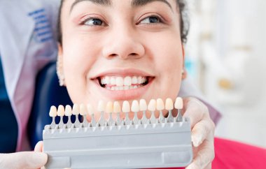 Diş hekimi farklı tonlarda implantlar tutuyor. Diş implantının gölgesini seçen hasta. Diş gölgesi seçimi, hastaya diş protezleri gösteren diş hekimi.