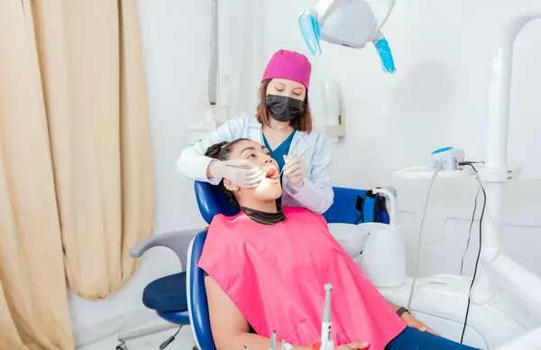 stock image Female dentist with probe and dental mirror examining mouth to lying patient. Health and dental care concept, Dentist doctor examining mouth to female patient lying on chair