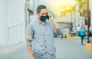 Cerrahi maskeli bir adam telefonla arıyor. Maskeli bir adam sokakta telefonla konuşuyor. Maskeli bir adam sokakta telefonla konuşuyor.