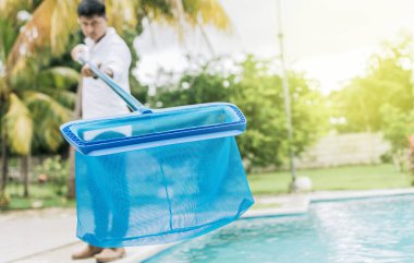 Person with skimmer cleaning pool. Man cleaning the pool with the Skimmer, A man cleaning pool with leaf skimmer. Hands holding a skimmer with blue pool in the background