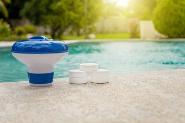 Tablets with chlorine dispenser for swimming pools. Chlorine tablets with dosing float, Pool float and chlorine tablets, A pool float and chlorine tablets on the edge of a swimming pool. clipart