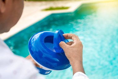 Hand of a pool disinfection worker holding a chlorine dispenser. Hands of a worker installing a pool chlorine float, a person holding a pool chlorine dispenser. Hands holding a pool chlorine dispenser. clipart