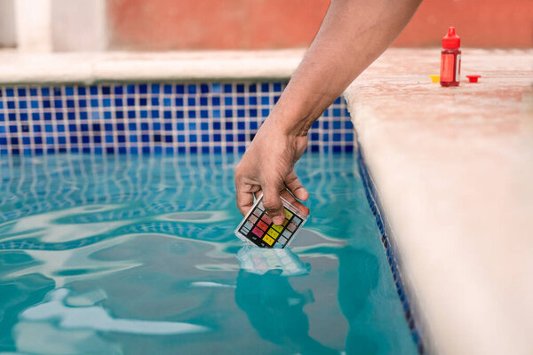 Закрыть лицо, проверяющее ph воды с мини-тестером в бассейне. Ручные испытания воды бассейна для хлора с PH мини-тестером. Тестирование хлора и рН бассейна
