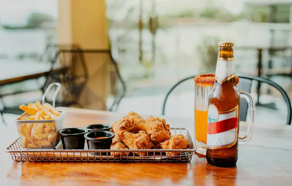 stock image Traditional spicy chicken wings with fries and michelada accompanied with beer served on wooden table