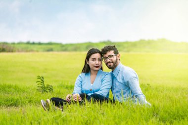 Sahada çimenlerde oturan aşık bir çiftin portresi, çimenlerde oturup kameraya bakan romantik bir çift, çimenlerde oturup kameraya bakan iki sevgili.