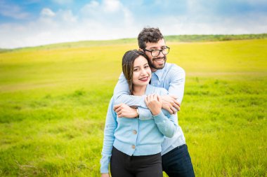 Sahada kucaklaşan mutlu bir çiftin portresi yeşil alanda birbirine aşık genç bir çiftin, kameraya bakan şirin bir çiftin portresi, kameraya bakan sevimli bir çiftin portresi.
