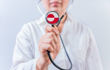 Grönland bayrağıyla steteskop tutan kadın doktor. Grönland Ulusal Sağlık Sistemi