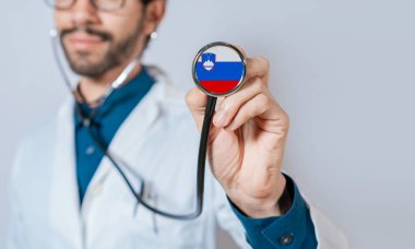 Slovenya bayrağıyla steteskop tutan doktor. Slovenya sağlık ve bakım kavramı, Slovenya bayrağı steteskopta