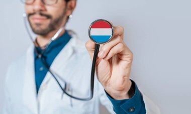 Doktor, Lüksemburg bayrağıyla steteskop tutuyor. Lüksemburg sağlık ve bakım konsepti, steteskopta Lüksemburg bayrağı
