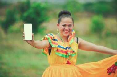 Geleneksel folklor kostümlü gülümseyen Latin kız ekranda telefonu gösteriyor. Geleneksel halk elbisesi içinde telefon ekranı gösteren Nikaragualı kız