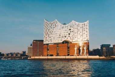 Hamburg 'daki Elbphilharmonie' nin modern mimari ve su yansımaları ile altın saat manzarası