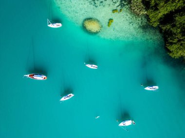 Worthersee 'nin turkuaz sularında yüzen yelkenlilerin canlı yeşil bir çevresi var..
