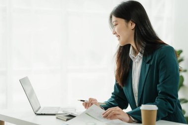 Finans kurumu çalışanı Asyalı kadınlar, görevlere dalmış profesyoneller. İş adamları özenle hesaplama yapar, müşterilere danışır ve masalarından anlaşma sağlarlar..