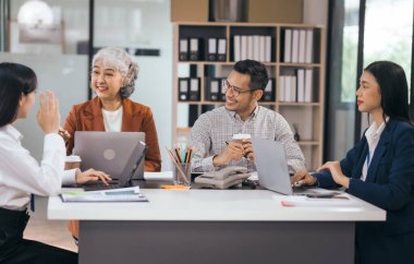 Dört Asyalı bir ofiste dizüstü bilgisayarlarla çalışıyor, görevleri tartışıyorlar. Katılımcıların görüşlerini paylaştığı ve tartıştıkları yıllık toplantı, takım çalışması grubunun laptopunu toplantı odasında sunumu