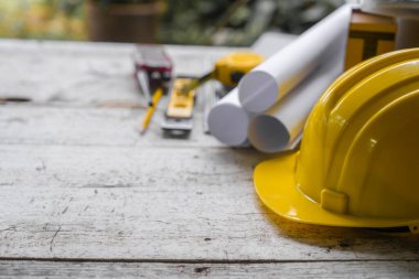 yellow safety helmet and rolled up architectural blueprints on a wooden desk, indicative of an architect's work area, possibly at a construction site. clipart