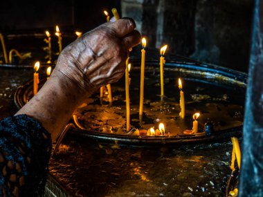 Yaşlı bir kadının eli kilisede mum yakıyor.