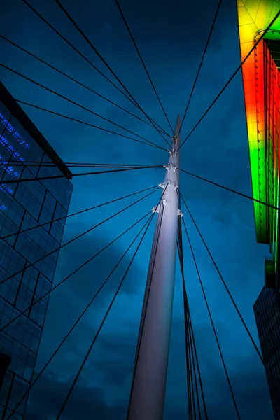 Upward perspective night photo of the Millennium Bridge nestled between to buildings in lower downtown Denver. 