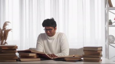 Evde eğitim. Okuyan adam. Mesafe çalışması. Aydınlık odada içi kitaplarla dolu bir masada oturan sıradan bir adam..
