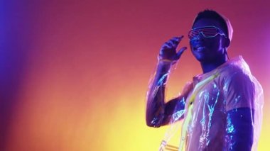 Siber punk modası. Neon insanları. Fütürist ilham. Plastik ceketli, parti gözlüklü, mor turuncu renkli, parlak reklam alanı arka planında göz kırpan kendine güvenen adam..