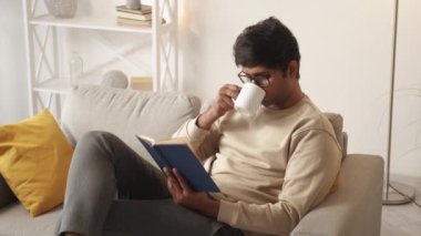 Evde rahatla. Okuyan adam. Eğlencenin tadını çıkarıyorum. Kitapla kahve içen mutlu sıradan bir adam. Koltuğun iç tarafında hafif bir odada oturuyor..