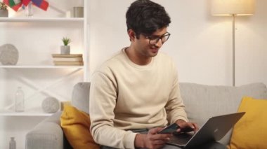 Çevrimiçi ödeme. Mutlu adam. Dijital teknoloji. Sıradan gülümseyen adam dizüstü bilgisayarda oturuyor. Kredi kartı gibi görünüyor. Koltukta oturuyor..