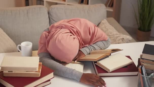彻底的教育 睡梦中的女人学习考试 疲惫的女士 头戴头巾 把书桌放在一堆书籍上 灯光下房间可以看到室内运动 — 图库视频影像
