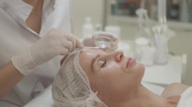 Güzellik prosedürü. Dişi cilt bakımı. Profesyonel kozmetik. Kozmetik uzmanı, açık kuaför salonunda orta yaşlı bir kadına jel maske takıyor..
