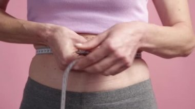 Bel kontrolü. Zayıf bir kadın. Kilo kaybı ölçüsü. Pembe arka planda, belinde mezura olan tanınmayan bir kadın..