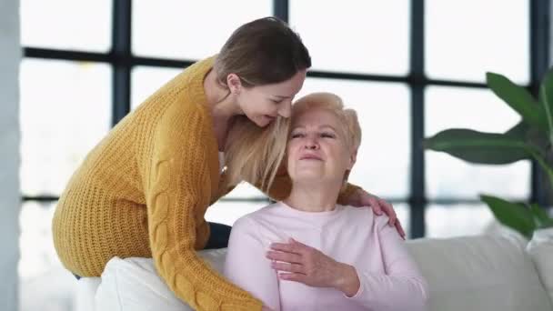 家庭之爱快乐的女人支持关系 坐在沙发灯室里 微笑着的女儿温柔地拥抱着母亲说话 — 图库视频影像