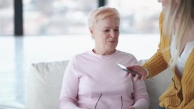 Yakın ilişki. Mutlu kadınlar. Taşınabilir anılar. İlham kaynağı kızın, aydınlatma odasındaki koltukta oturan ilgili anneye akıllı telefondan fotoğraf göstermesi..