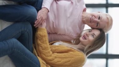 Dikey video. Aile desteği. Dikkatli kadınlar. Anın tadını çıkar. Şefkatli anne, kızı kucaklıyor, evdeki aydınlık odada kanepede oturuyor..