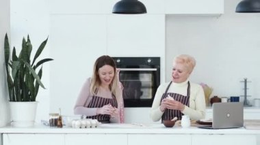 Aile eğlencesi. Mutlu kadınlar. Tatil fırını. Neşeli anne ve kız dans ediyor ve şarkı söylüyor. Mutfak odasının iç tarafında hamur işi pişirirken..