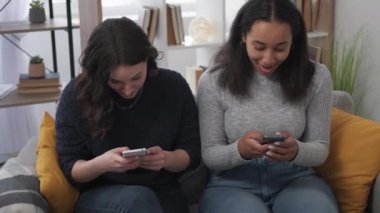 Kazanan neşe. Heyecanlı kadınlar. Cep telefonu bilgileri. Şaşırmış bayan arkadaşlar kutlama yapıyorlar. Akıllı telefon görünümlü, kanepede, aydınlık odada oturuyor..