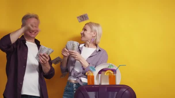 旅の費用だ 金持ちのカップル 休暇の喜び 幸せな中年男性と女性Spreading現金ドル周りPosingとともに荷物上の黄色の背景スローモーション — ストック動画