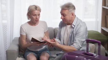Tatil heyecanı. İlham verici bir çift. Seyahat planı. Orta yaşlı mutlu adam ve kadın valiz lambasıyla evde oturarak notlar alıyorlar..