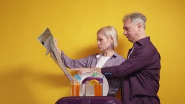 Kayıp gezgin. Aile çifti. Tatil seyahati. Orta yaşlı adam ve kadın haritada çalışıyor. Yeni ülke sarı arka planda bavulla poz veriyor..