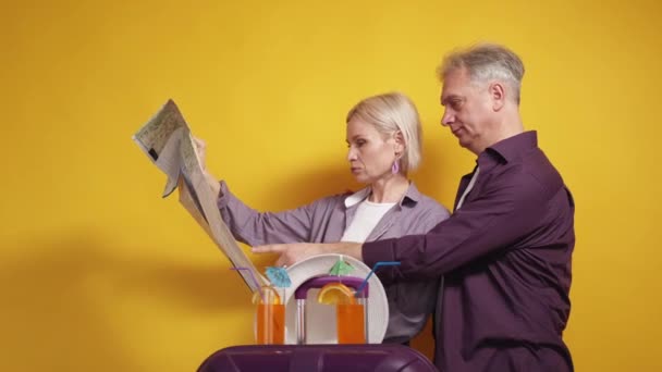 道に迷った 家族のカップル 休暇の旅 中年男性と女性勉強地図新しいです国ポーズとともに手荷物上の黄色の背景 — ストック動画