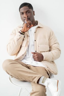 Kendine güvenen adam portresi. Sessiz jest. Bej kıyafetli modacı stüdyoda oturuyor.