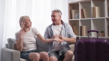Tatil heyecanı. Mutlu bir çift. Yolculuk ilhamı. Orta yaşlı bir adam ve kadın zevkle dans ediyor bavul valiziyle koltukta oturuyor ışık odası iç çekimde ağır çekim.